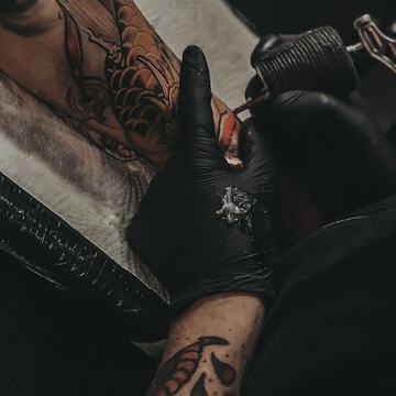 Тату-майстер працює над татуюванням на нозі